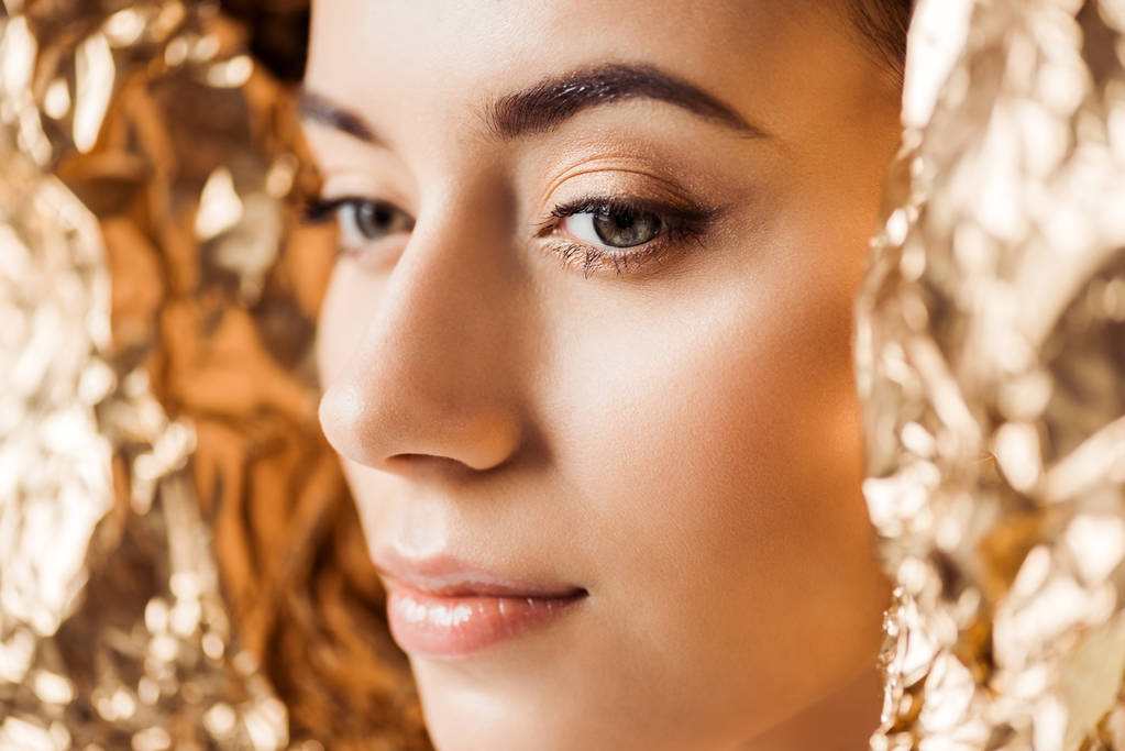 retrato de mujer atractiva joven con maquillaje brillante cerca de lámina de oro
  - Foto, imagen