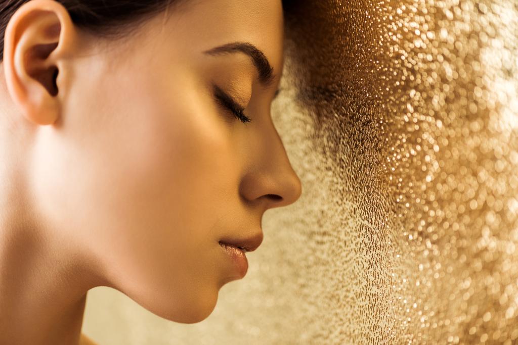 молодая красивая женщина с закрытыми глазами и блестящий макияж на золотом текстурированном фоне
 - Фото, изображение