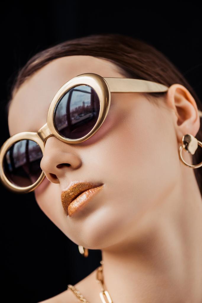 young woman in sunglasses, golden earring and necklaces isolated on black - Photo, Image