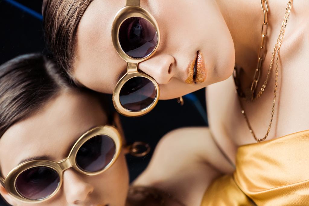 young woman in sunglasses, golden necklaces lying on mirror  - 写真・画像