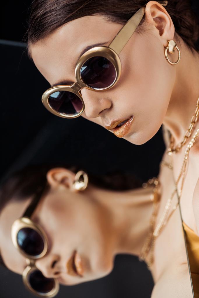 jonge stijlvolle vrouw in een zonnebril, gouden sieraden houden spiegel in de buurt gezicht - Foto, afbeelding