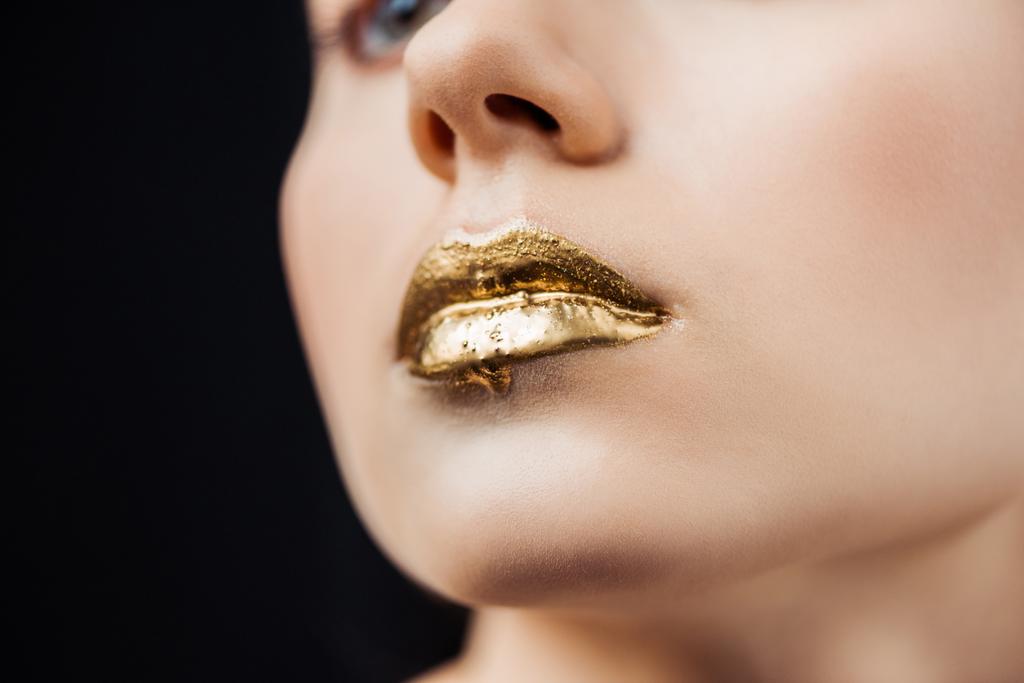 黒で隔離された金色の塗装された唇を持つ若い女性のトリミングされたビュー - 写真・画像