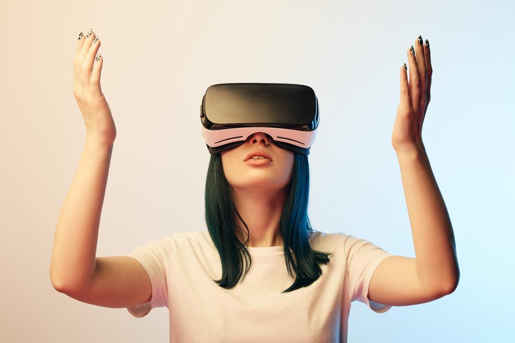 attractive young woman gesturing while wearing virtual reality headset on beige and blue  - Photo, Image