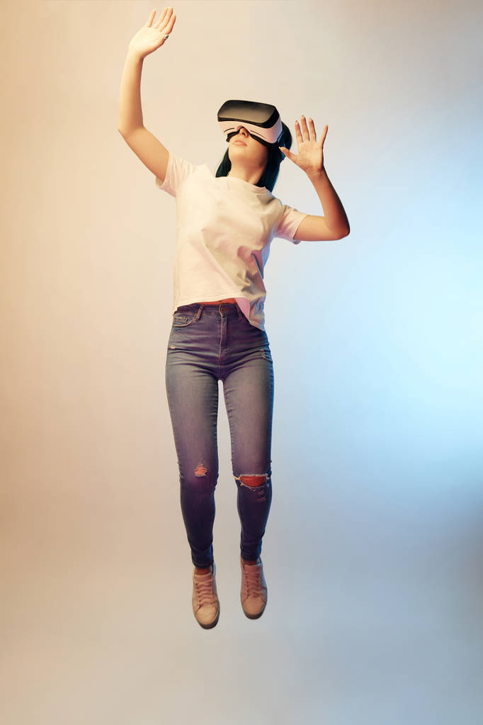 young woman in virtual reality headset gesturing while levitating on beige and blue  - Photo, Image