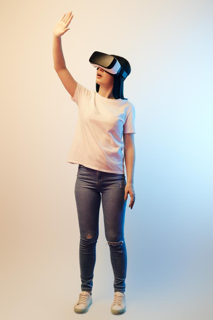 brunette young woman in virtual reality headset standing and gesturing on beige and blue  - Photo, Image