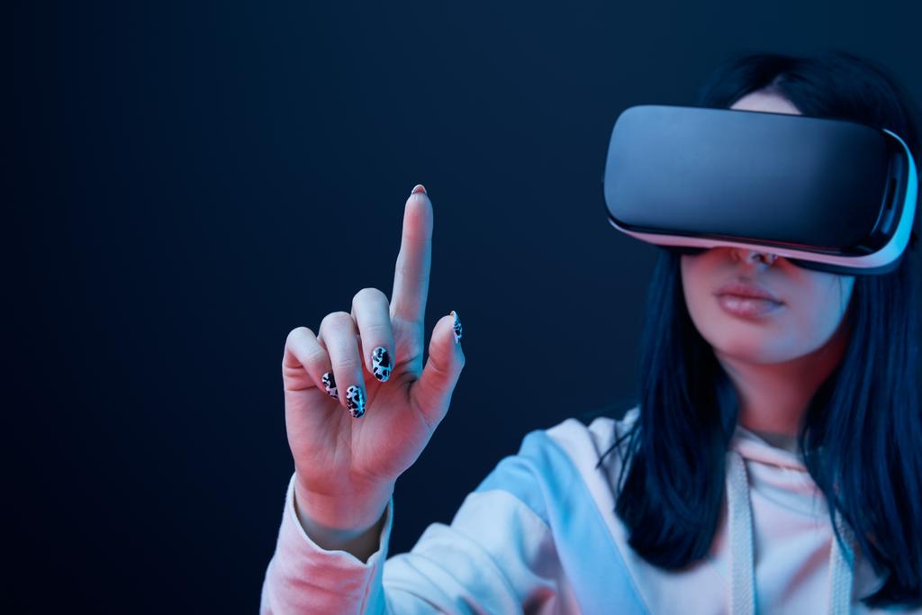 messa a fuoco selettiva della giovane donna bruna che indossa cuffie di realtà virtuale e punta con il dito sul blu
  - Foto, immagini