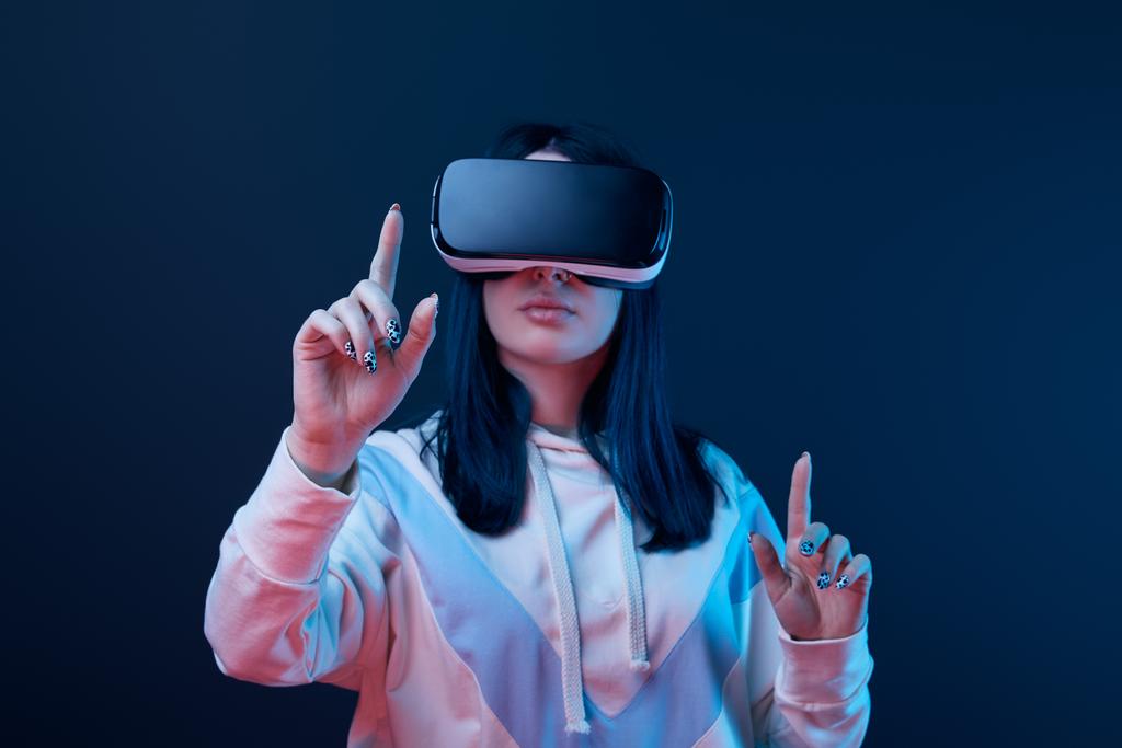 selectieve focus van jonge brunette vrouw dragen Virtual Reality headset en wijzend met de vingers op blauw  - Foto, afbeelding