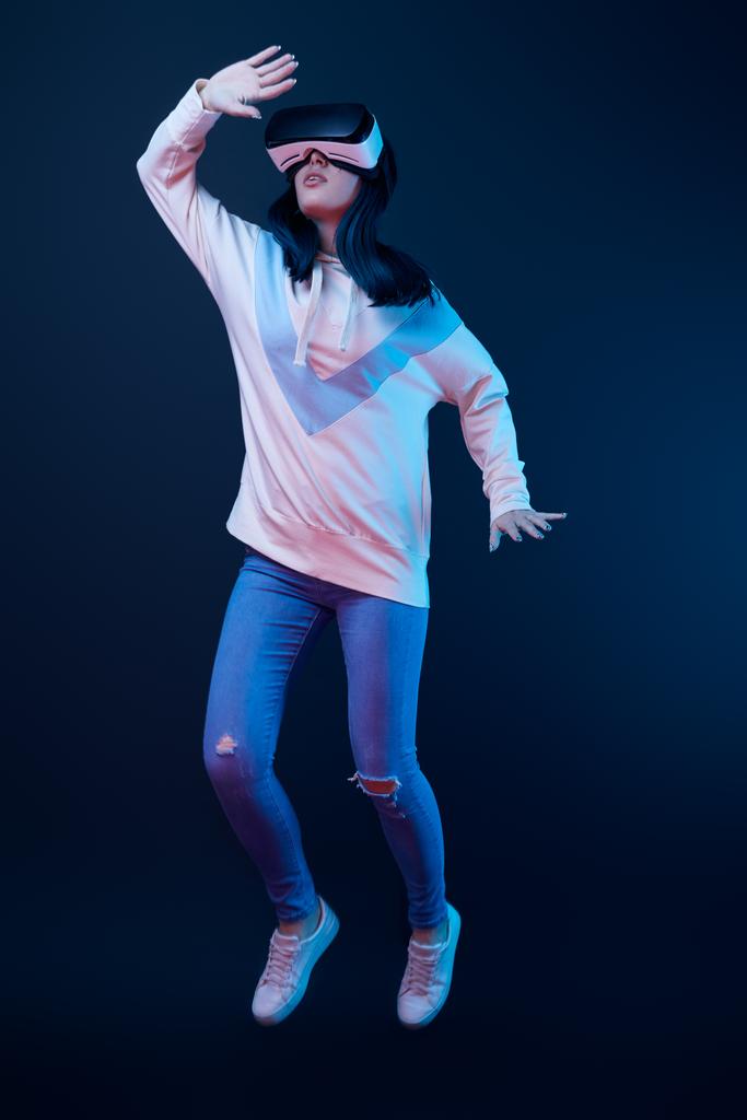junge Frau gestikuliert mit Virtual-Reality-Headset und springt auf blau  - Foto, Bild