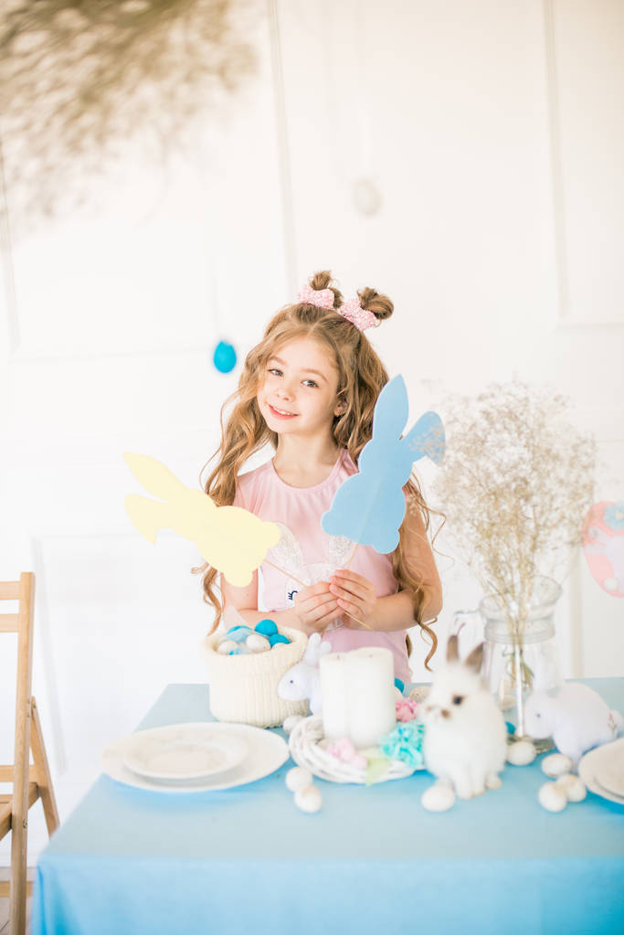 Petite fille mignonne avec de longs cheveux bouclés avec des petits lapins et décor de Pâques à la maison à la table de vacances
. - Photo, image