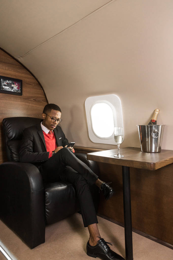 Επιτυχημένος νέος Αφροαμερικανός μαύρος επιχειρηματίας που κάθεται στην καρέκλα του ιδιωτικού του τζετ - Φωτογραφία, εικόνα