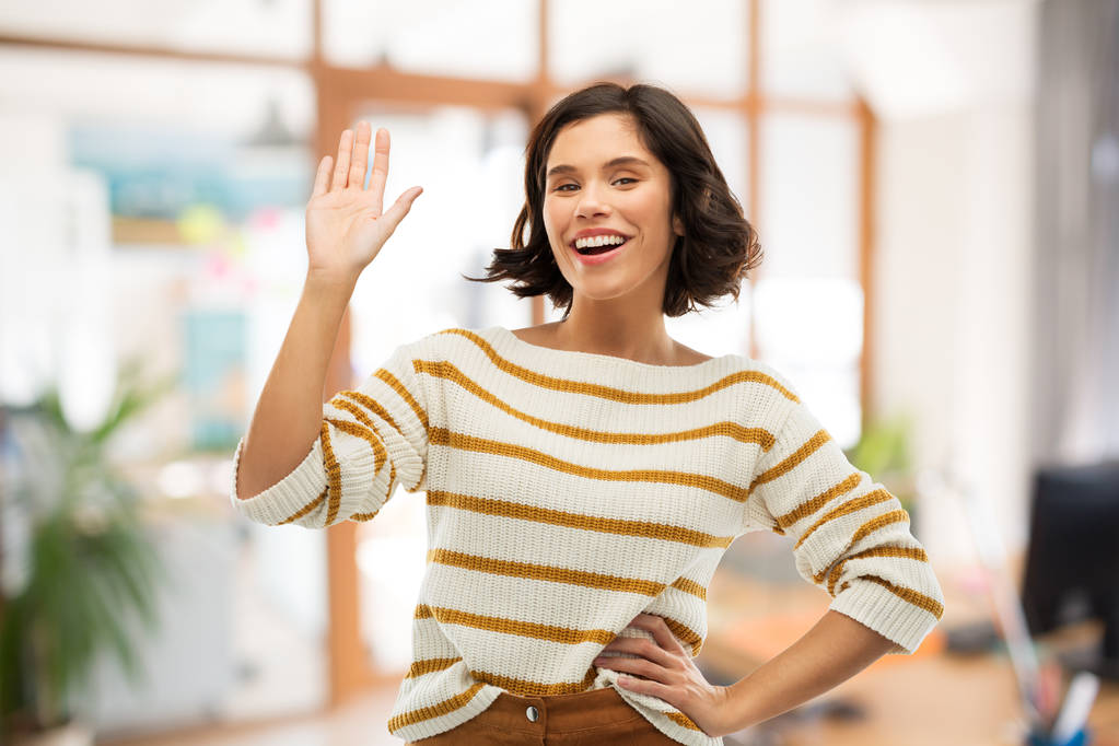 Glimlachende vrouw in gestreepte Pullover zwaaiende hand - Foto, afbeelding