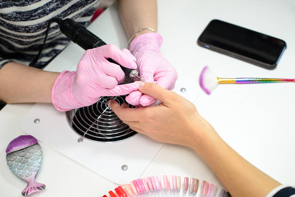Closeup shot of a woman in a nail salon receiving a manicure by a beautician with electric nail file. Woman getting nail manicure. Beautician file nails to a customer. - Photo, Image