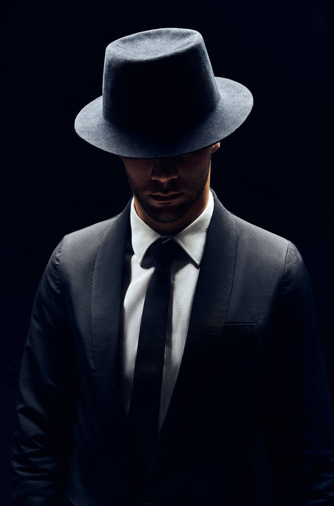 Beau homme confiant en costume noir et chapeau sur fond sombre. Homme concept de beauté
                                 - Photo, image
