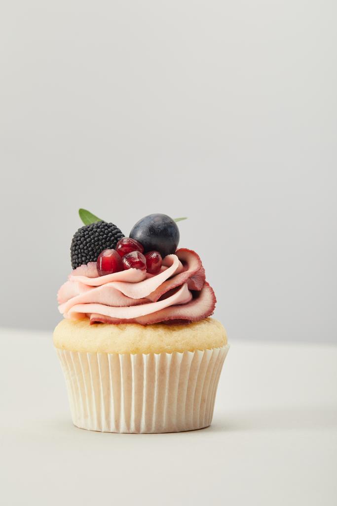 cupcake with grape, garnet and blackberry isolated on grey - Photo, Image