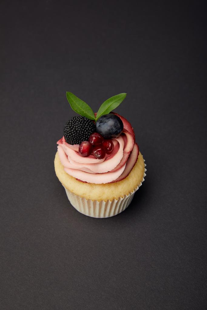 cupcake met room, granaat, druif en BlackBerry op zwart oppervlak - Foto, afbeelding