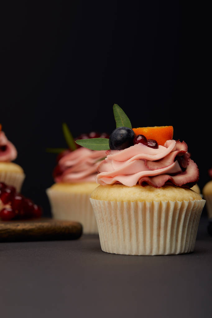 cupcakes with fruits and berries on grey surface isolated on black - Photo, Image