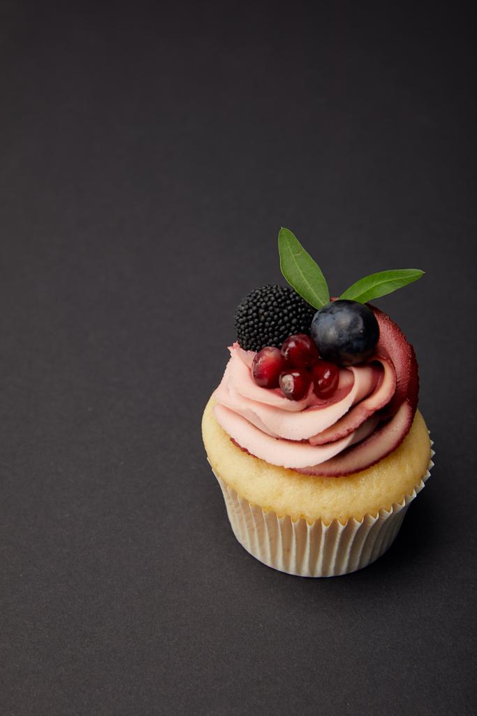 cupcake with garnet, blackberry and grape on black surface - Photo, Image