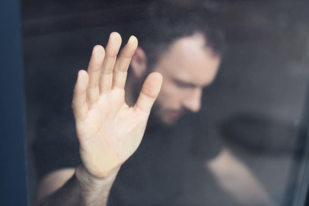 επιλεκτική εστίαση του απογοητευμένο άνθρωπο που κρατά το χέρι στο τζάμι του παραθύρου  - Φωτογραφία, εικόνα