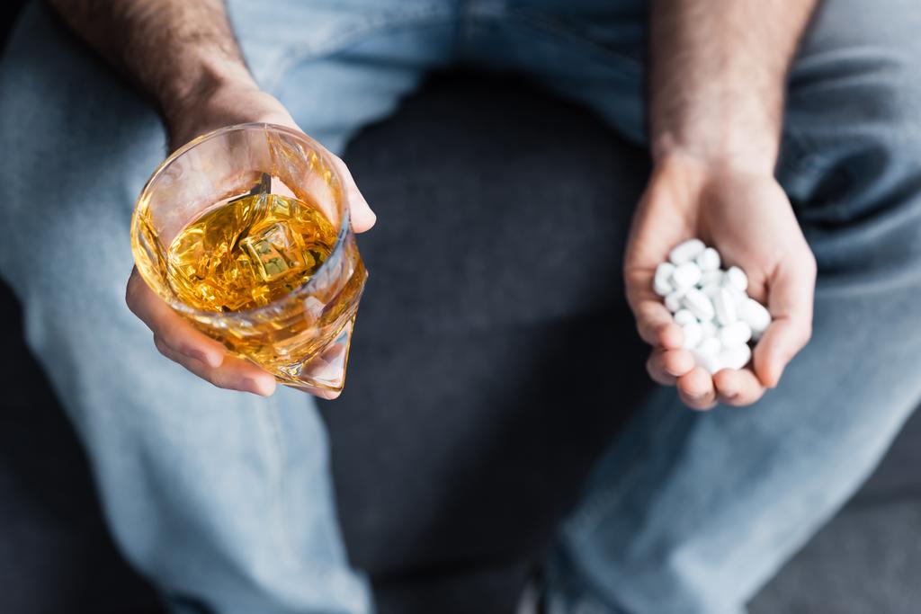 gedeeltelijke weergave van de man die glas whisky en handvol pillen vasthoudt - Foto, afbeelding