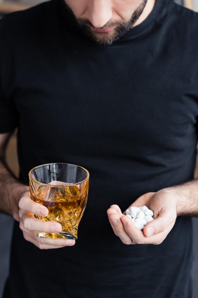 osittainen näkymä seisova mies musta t-paita tilalla lasi viskiä ja kourallinen pillereitä
 - Valokuva, kuva