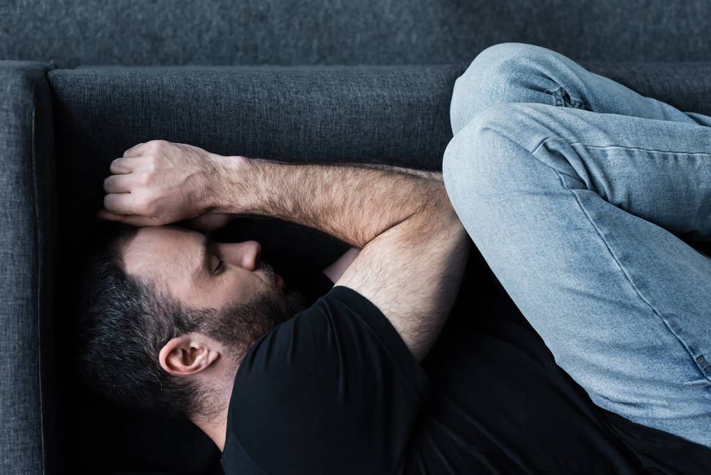 Widok z góry na depresję Brodatego mężczyzny cierpiącego podczas leżącej na kanapie z zamkniętymi oczami - Zdjęcie, obraz