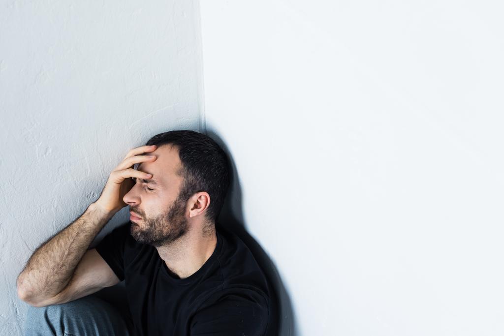 depressed man sitting in corner with closed eyes and holding hand on forehead - Photo, Image
