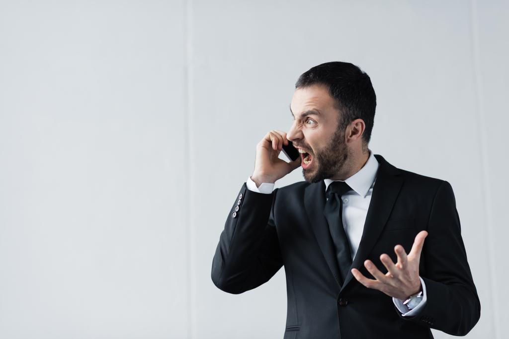 θυμωμένος επιχειρηματίας σε μαύρο κοστούμι καυγαδίζει ενώ μιλάει στο smartphone - Φωτογραφία, εικόνα