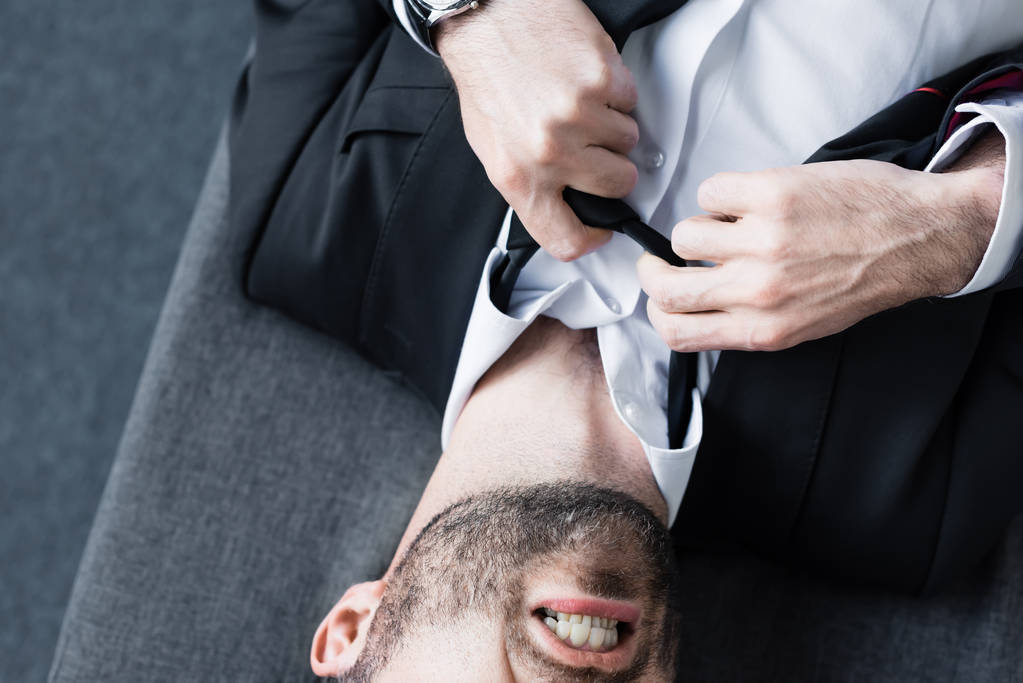 vista parcial del hombre de negocios deprimido que sufre y desata la corbata mientras está acostado en el sofá
 - Foto, imagen