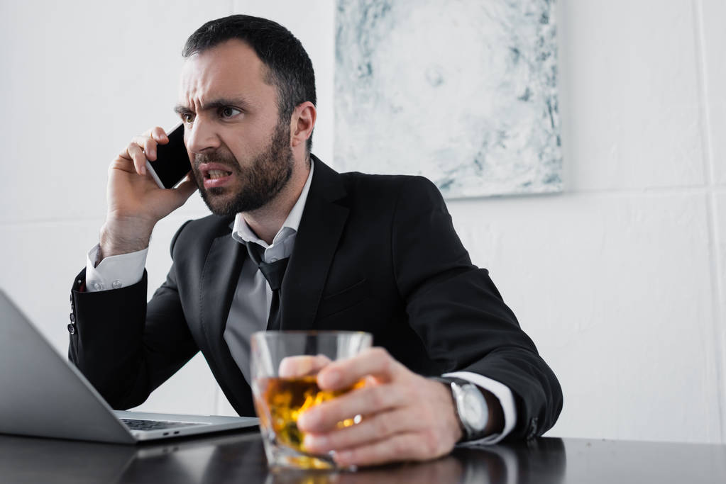 foco seletivo de homem de negócios zangado brigando enquanto fala no smartphone e segurando um copo de uísque
 - Foto, Imagem