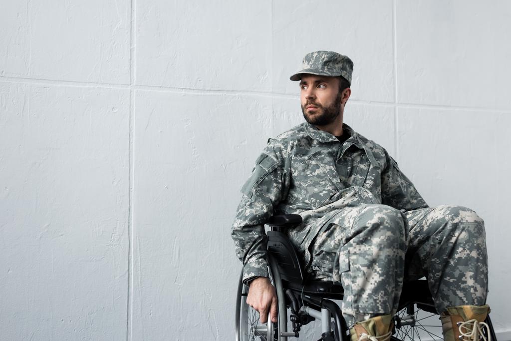 Nachdenklicher behinderter Soldat in Uniform sitzt im Rollstuhl und schaut weg - Foto, Bild