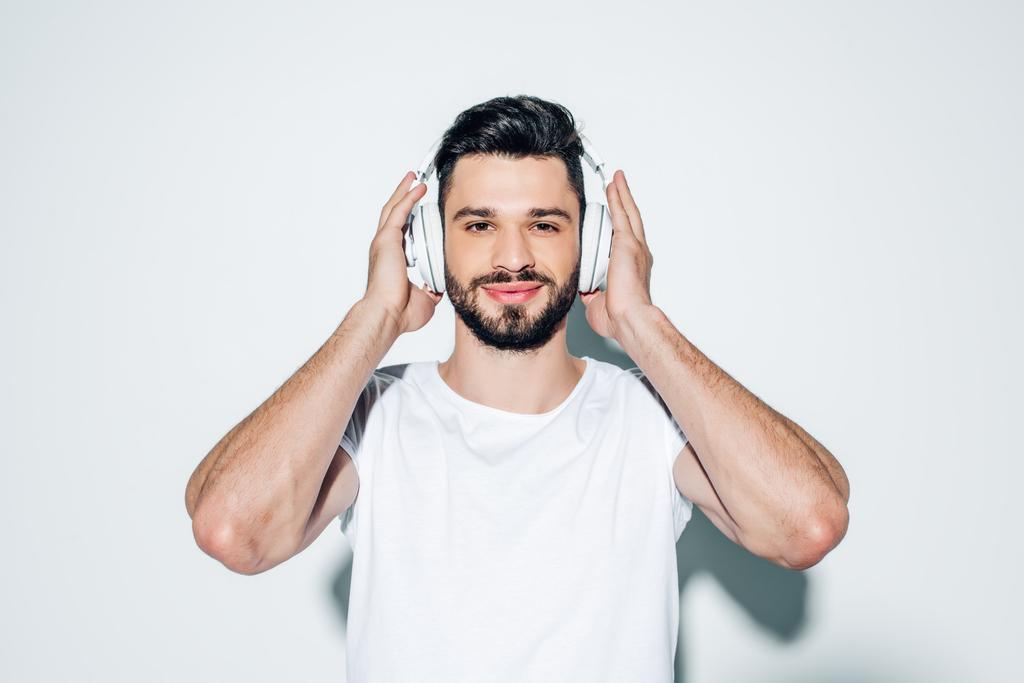 χαρούμενος άνθρωπος αγγίζοντας τα ακουστικά, ακούγοντας μουσική και χαμογελά στο λευκό  - Φωτογραφία, εικόνα
