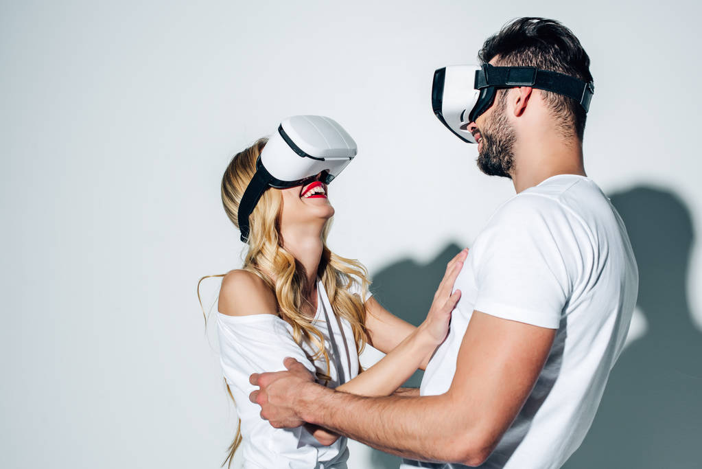 szczęśliwy człowiek dotykając blond kobieta podczas noszenia wirtualny zestaw słuchawkowy rzeczywistość na białym  - Zdjęcie, obraz