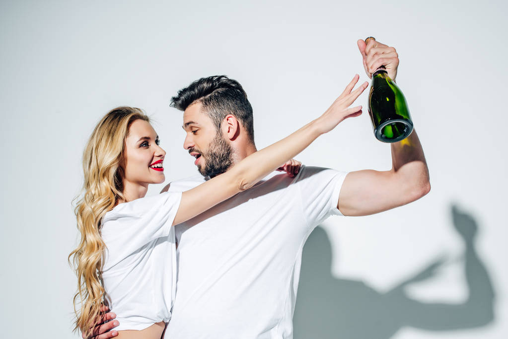 glückliche junge Frau blickt auf eine Flasche Champagner in der Hand eines hübschen Mannes auf Weiß  - Foto, Bild