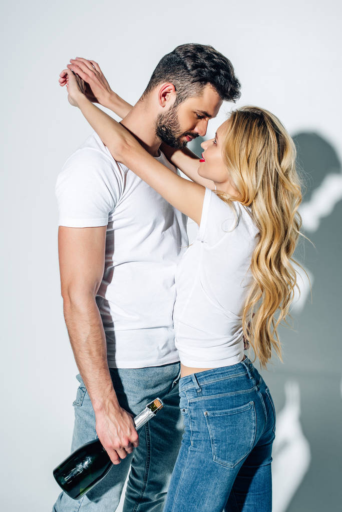 blonde jonge vrouw knuffelen knappe man met fles champagne op wit  - Foto, afbeelding