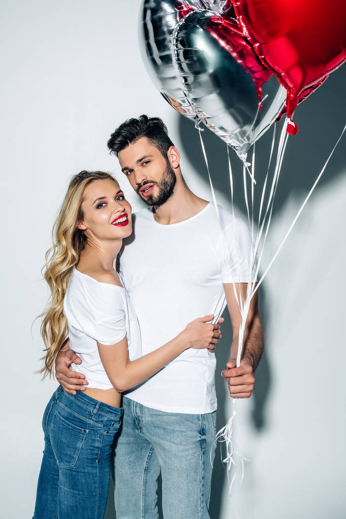cheerful woman hugging handsome man holding balloons on white  - Photo, Image