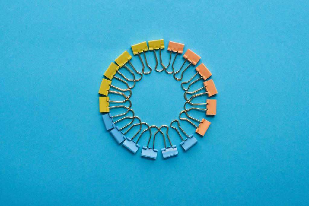 bovenaanzicht van paperclips gerangschikt in ronde vorm geïsoleerd op blauw - Foto, afbeelding
