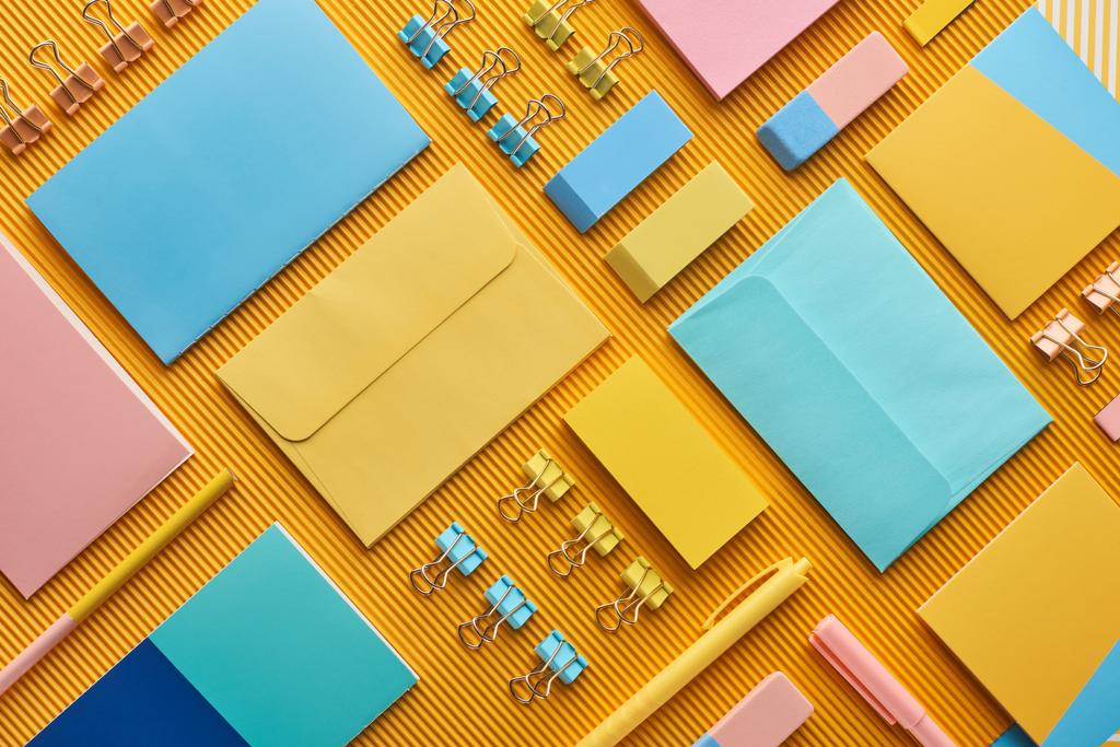 плоская раскладка разноцветных канцелярских принадлежностей для офиса на желтом
 - Фото, изображение