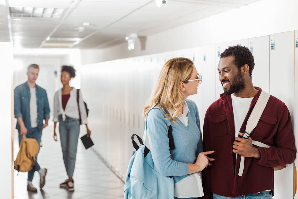 sorrindo estudantes multiétnicos olhando uns para os outros no corredor na faculdade
 - Foto, Imagem