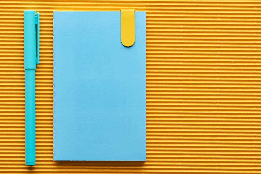 επάνω όψη της μπλε πένας και του σημειωματαρίου σε κίτρινο με χώρο αντιγραφής - Φωτογραφία, εικόνα