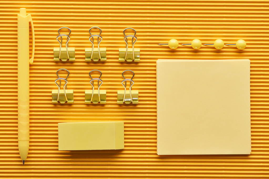 верхний вид ручки, скрепки и разноцветные канцтовары для офиса на желтый цвет
 - Фото, изображение