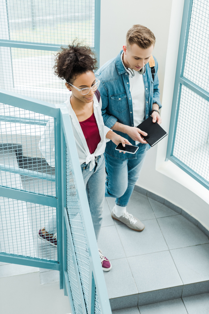 overhead view of two students with notebook and smartphone standing on stairs - Photo, Image