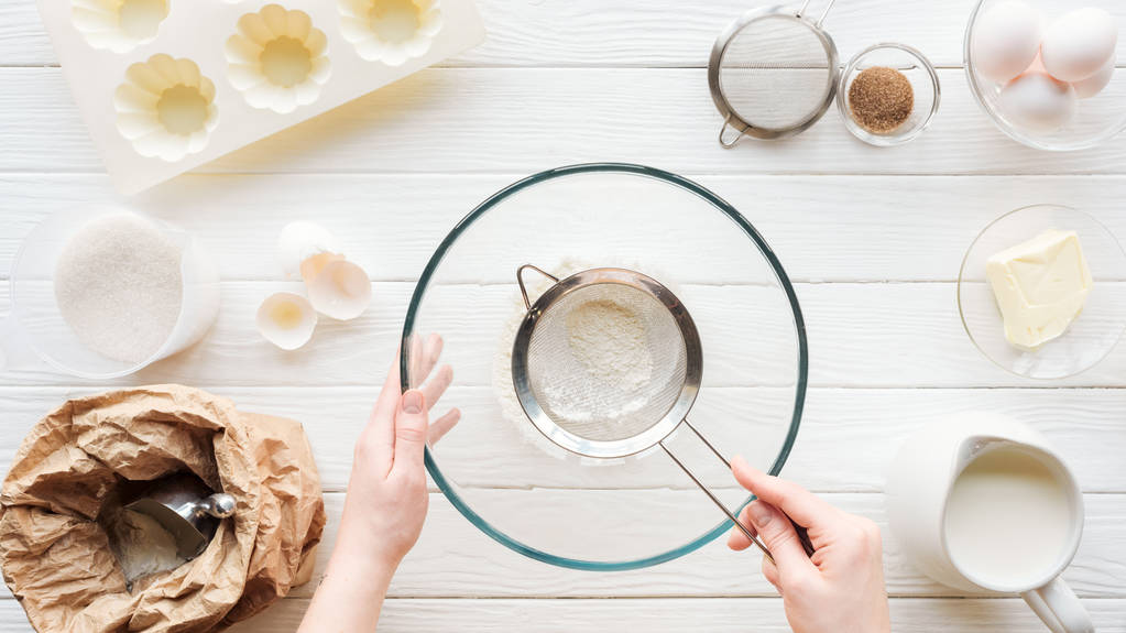 visão parcial da mulher peneirando farinha na tigela na mesa com ingredientes
 - Foto, Imagem