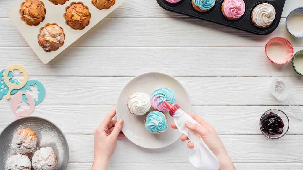 vista parziale di donna decorazione cupcakes con sacchetto di glassa sul tavolo con vassoi cupcake
 - Foto, immagini