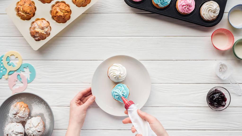 cupcake tepsileri ile masada buzlanma torbası ile kadın dekorasyon cupcakes kısmi görünümü - Fotoğraf, Görsel
