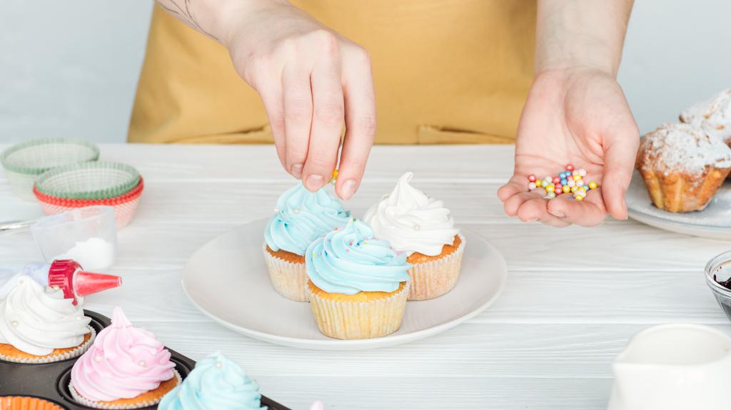 abgeschnittene Ansicht einer Frau, die Cupcakes mit Streusel dekoriert - Foto, Bild