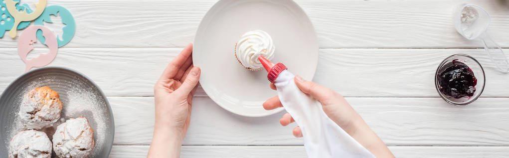 plano panorámico de mujer decorando cupcake con bolsa de hielo en mesa de madera blanca
 - Foto, imagen