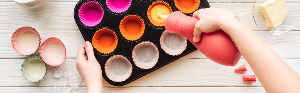 panoramic shot of woman pouring liquid dough in cupcake pan on table - Photo, Image