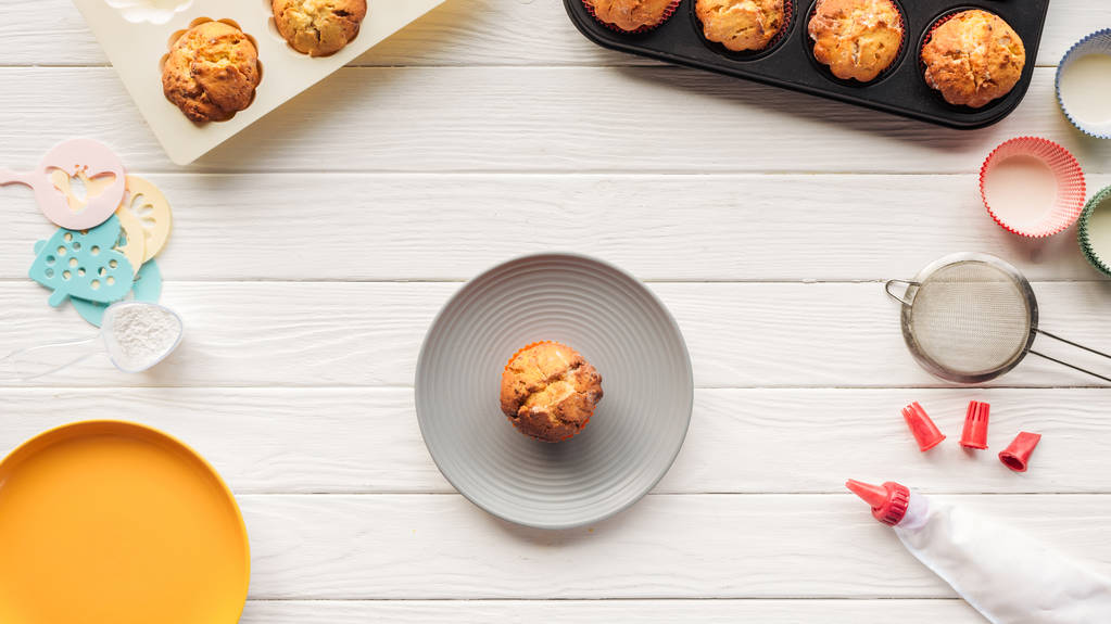 Draufsicht auf leckere Muffins in Blechen und Backwerkzeugen auf Holztisch - Foto, Bild