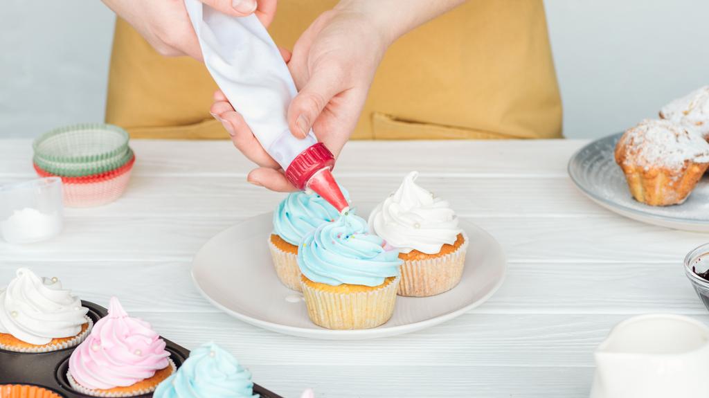 Teilansicht einer Frau, die Cupcakes mit Zuckerguss verziert - Foto, Bild