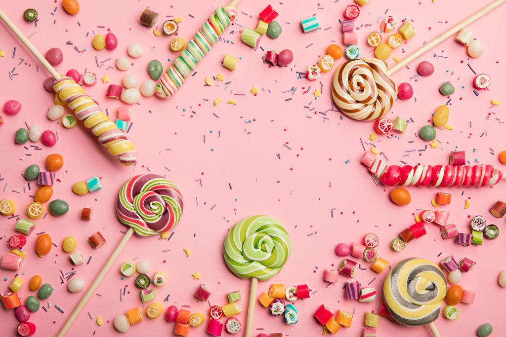 вид сверху на вкусные разноцветные леденцы, карамельные конфеты и брызги на розовом фоне
 - Фото, изображение
